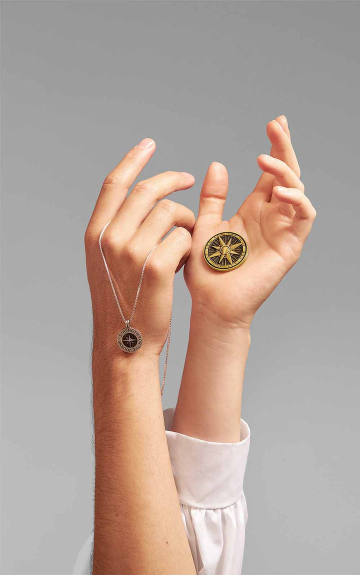 Two hands intertwined in the air holding a handmade traveling Talisman and a traveling Pendant